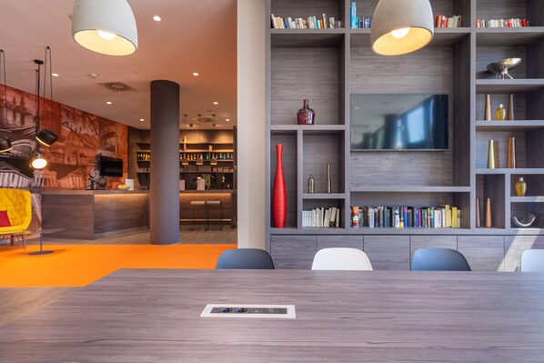 Una sala de conferencias moderna con una mesa de madera, una amplia estantería y una televisión.