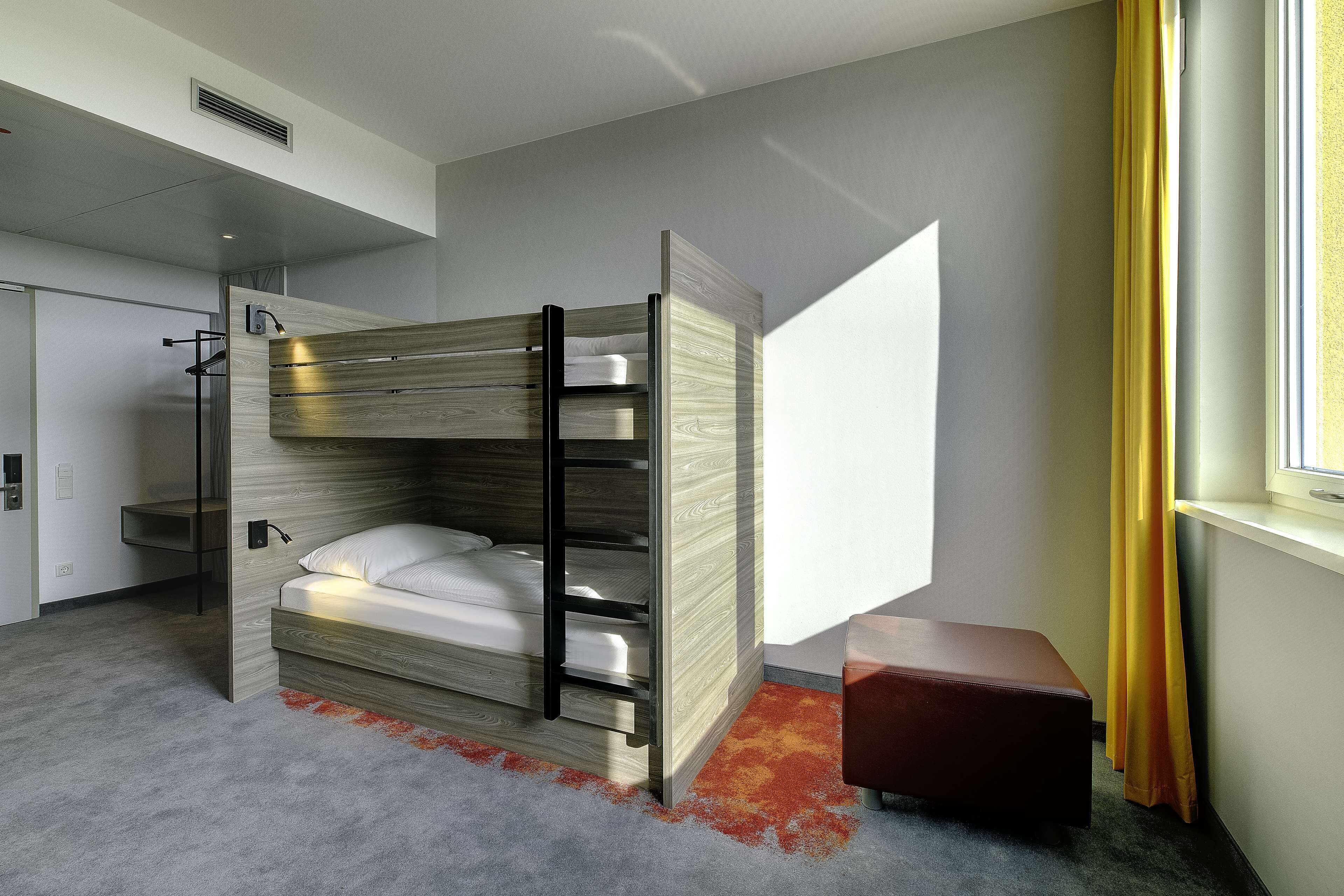 Et moderne hotelværelse med køjeseng, et lille skrivebord og et vindue med gardiner.