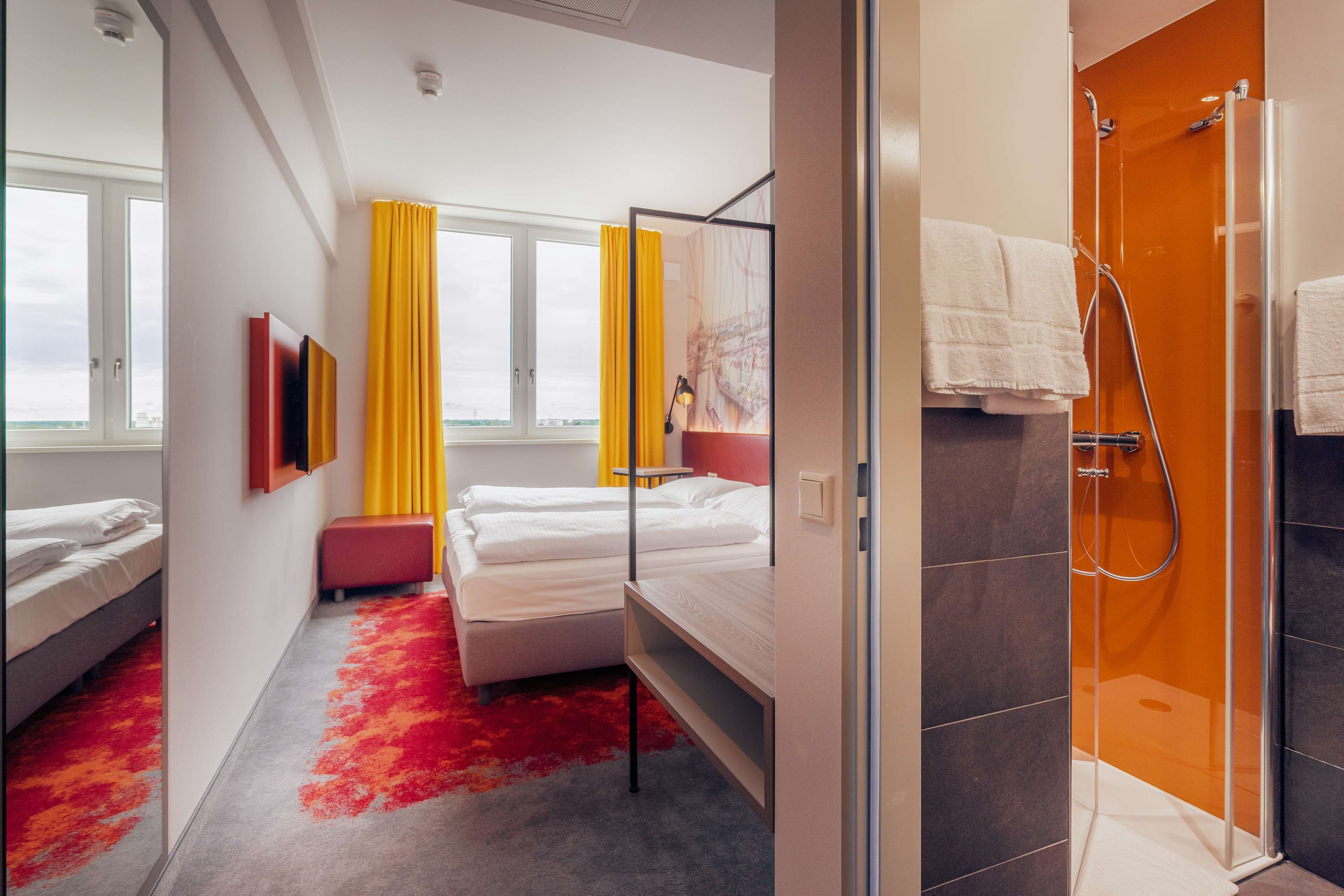 Une chambre d’hôtel avec un lit, une banquette, une douche et une fenêtre avec des rideaux.