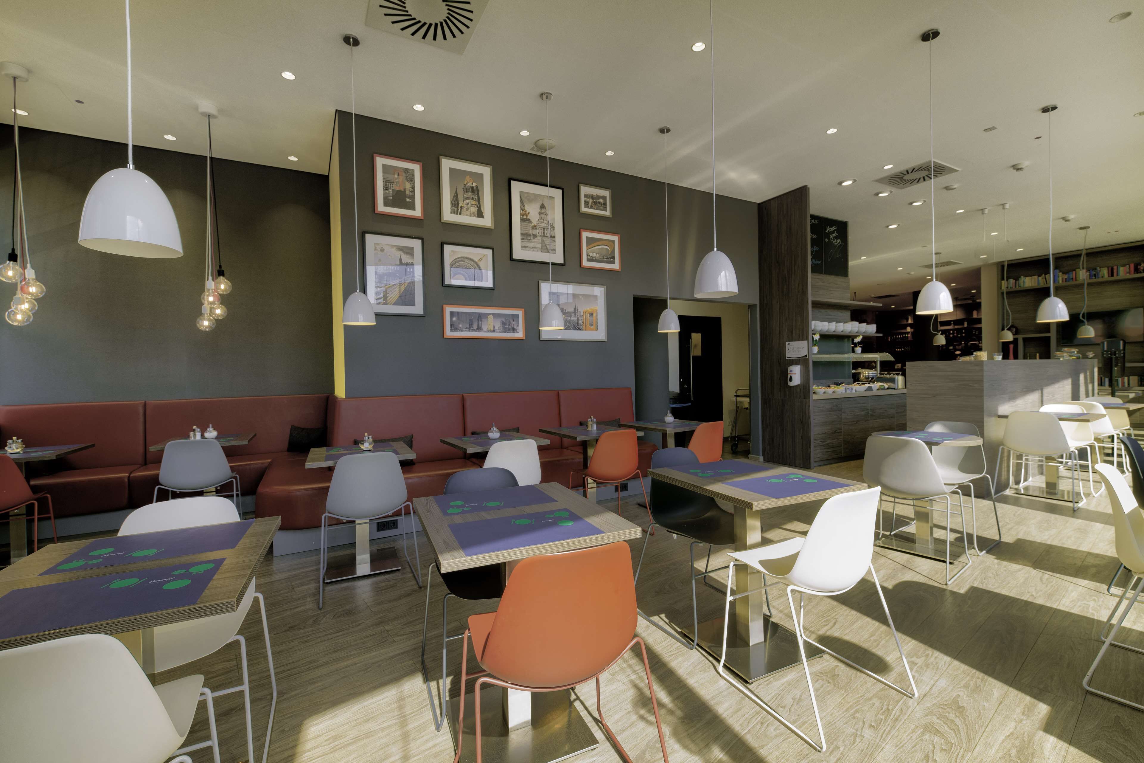 Un restaurante moderno con cabinas, mesas y sillas, que presenta obras de arte en las paredes e iluminación colgante.