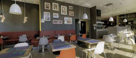 A modern restaurant with booths, tables, and chairs, featuring artwork on the walls and pendant lighting.