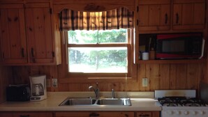 A kitchen with wooden cabinets, a window, a microwave, a stove, and a coffee maker. - Pet-Friendly Cabin On The Lake With Fireplace (St. Germain)