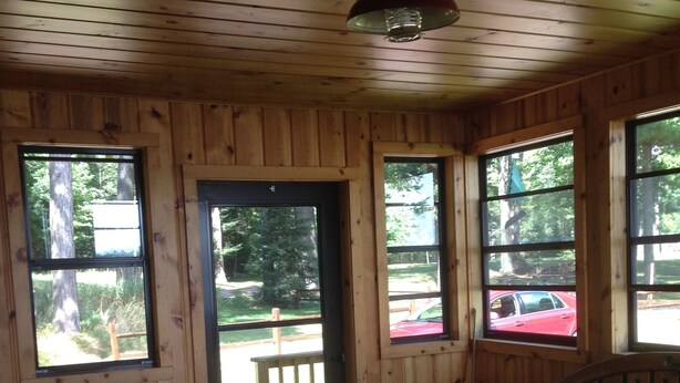 A cabin interior with wooden walls, a bench, a table, and large windows offering views of the outside. - Pet-Friendly Cabin On The Lake With Fireplace (St. Germain)
