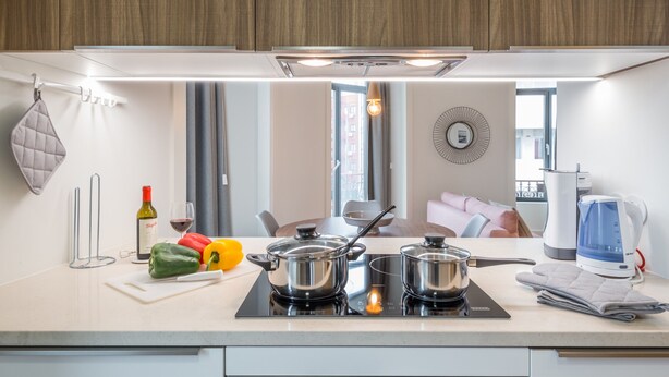 Een moderne keuken met een wit aanrecht, twee inductiekookplaten, een waterkoker en een eethoek met een tafel en stoelen.