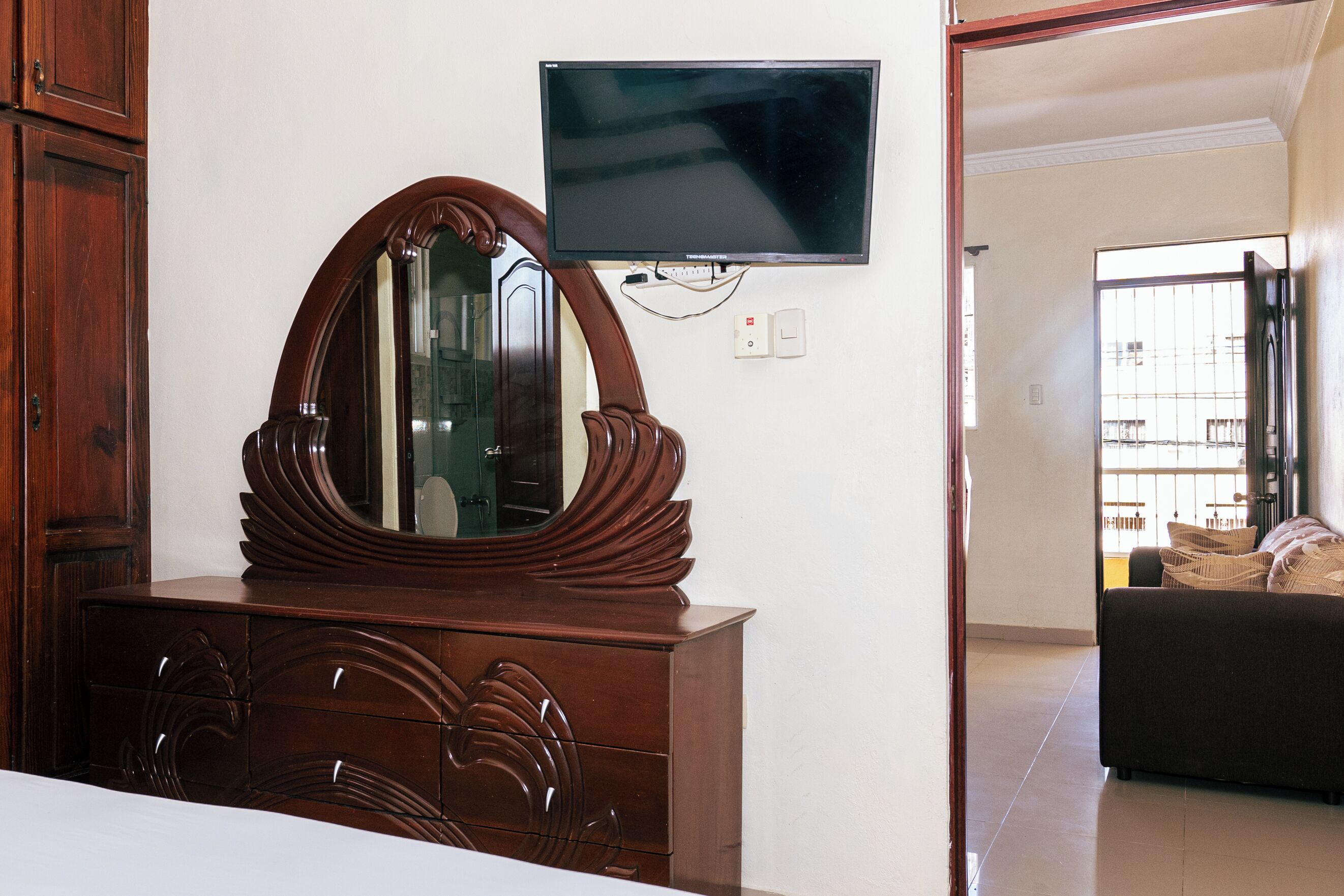 A room with a wooden dresser, a flat-screen TV mounted on the wall, and a view of an outdoor balcony.