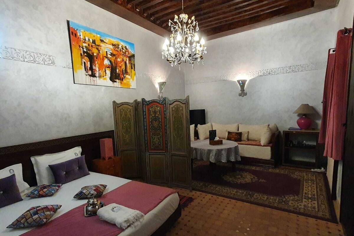 Un dormitorio con una cama, un sofá, una araña y un cuadro en la pared.