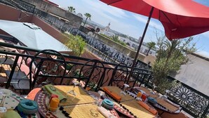 A rooftop terrace with tables set up for dining, surrounded by decorative plants and a red umbrella. - Riad La Porte Du Bouregreg (Salé)
