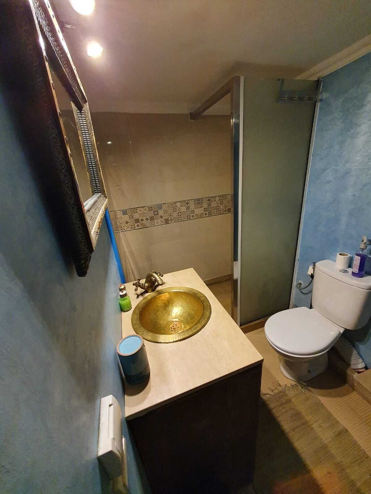 A bathroom with a gold sink, white toilet, and a glass shower enclosure.