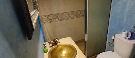 A bathroom with a gold sink, white toilet, and a glass shower enclosure.