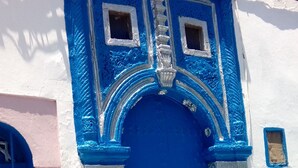A building with a blue door, white walls, and a small window. - Riad La Porte Du Bouregreg (Salé)