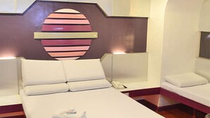 A hotel room with a bed, a bedside table, a nightstand, and a wall-mounted light fixture. - Astrotel Anonas (Quezon City)
