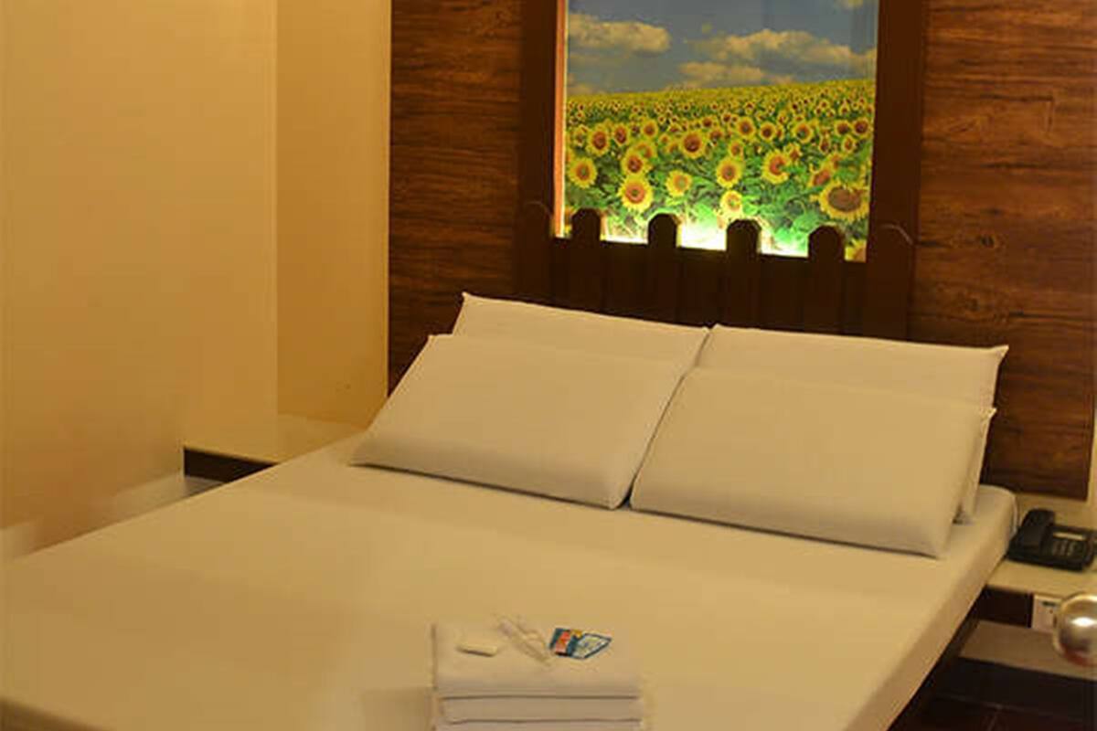 A neatly made bed with white linens and pillows, a folded towel on the bed, and a wooden headboard.