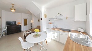 A modern kitchen with white cabinets, a wooden countertop, and a sink. There is a dining area with a white table and chairs, and a TV in the living room.