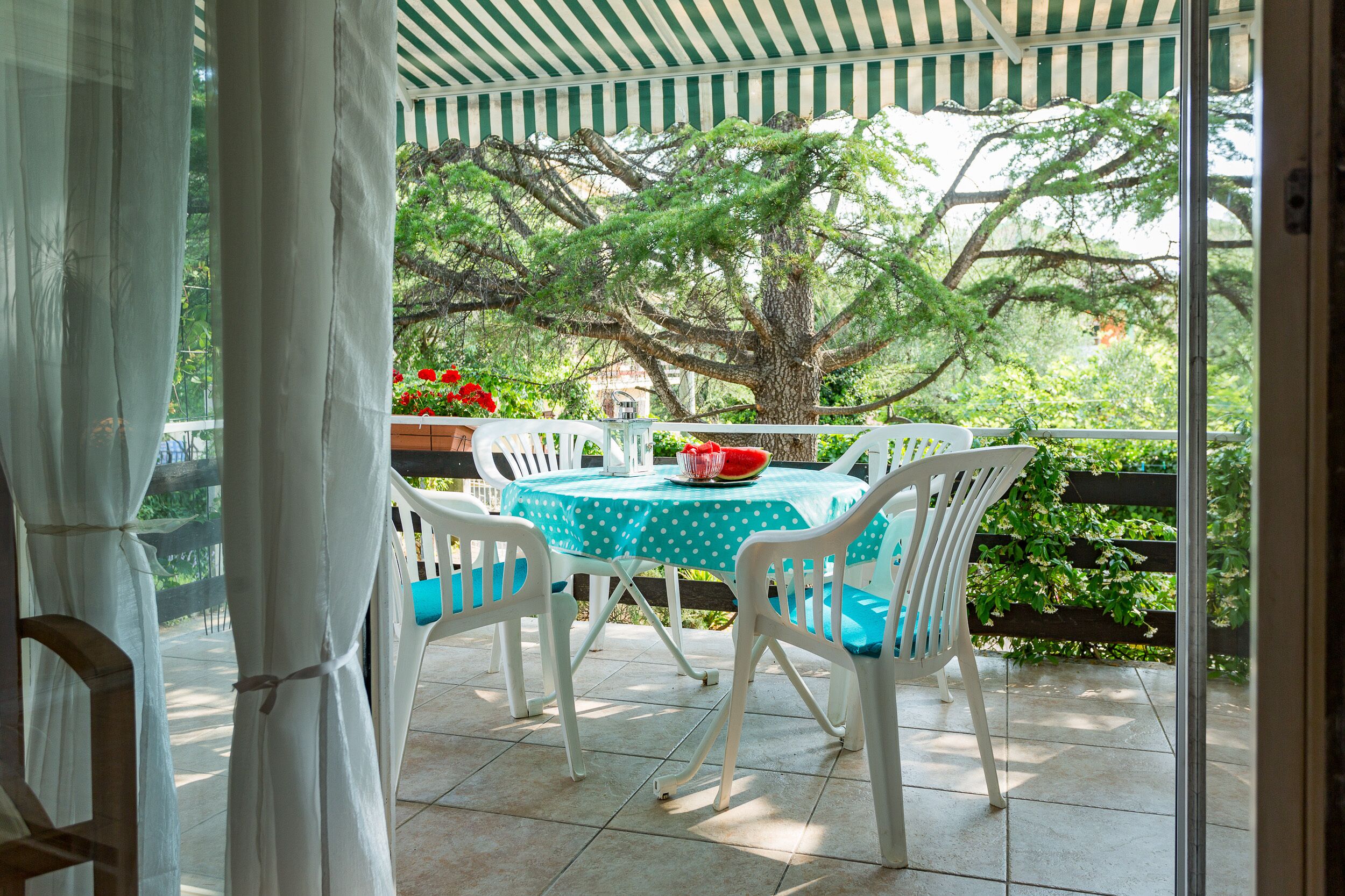 An outdoor patio with a table and chairs, a view of trees, and a covered area with a striped awning.