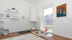 A modern kitchen with white cabinets, a wooden countertop, a built-in dishwasher, and a window with a view of trees.