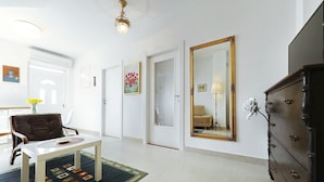 A room with a white wall, a large mirror, a dark wooden dresser, a white table with a patterned rug, and a brown leather chair.