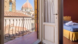 A balcony with a wrought iron railing, a bed with a blue and yellow bedspread, and a view of a historic building with a dome.