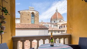 A balcony with a table, a bottle of champagne, and a view of historic buildings.