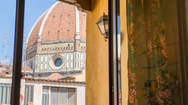 A view of a building with a dome and a circular window, through a window with a floral curtain.
