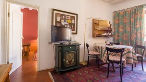 A room with a television on a cabinet, a dining table with chairs, a patterned rug, and a floral curtain.