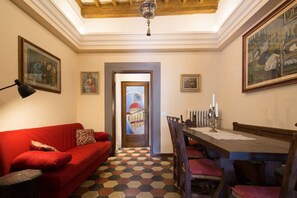 A room with a red sofa, a dining table with chairs, a chandelier, and a checkered floor.