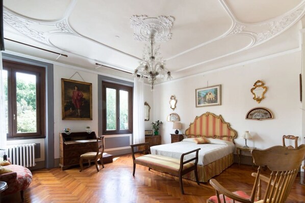 A bedroom with a bed, a desk, a chair, a chandelier, and a window.