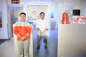Three individuals standing in a hotel reception area with a digital clock displaying 12:58:38. - Astrotel Guadalupe (Makati)