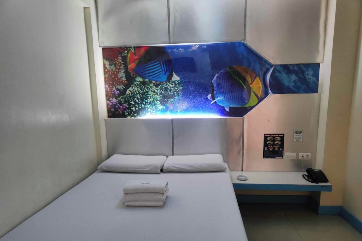 Une chambre d’hôtel avec un lit, une table de chevet et un aquarium fixé au mur.