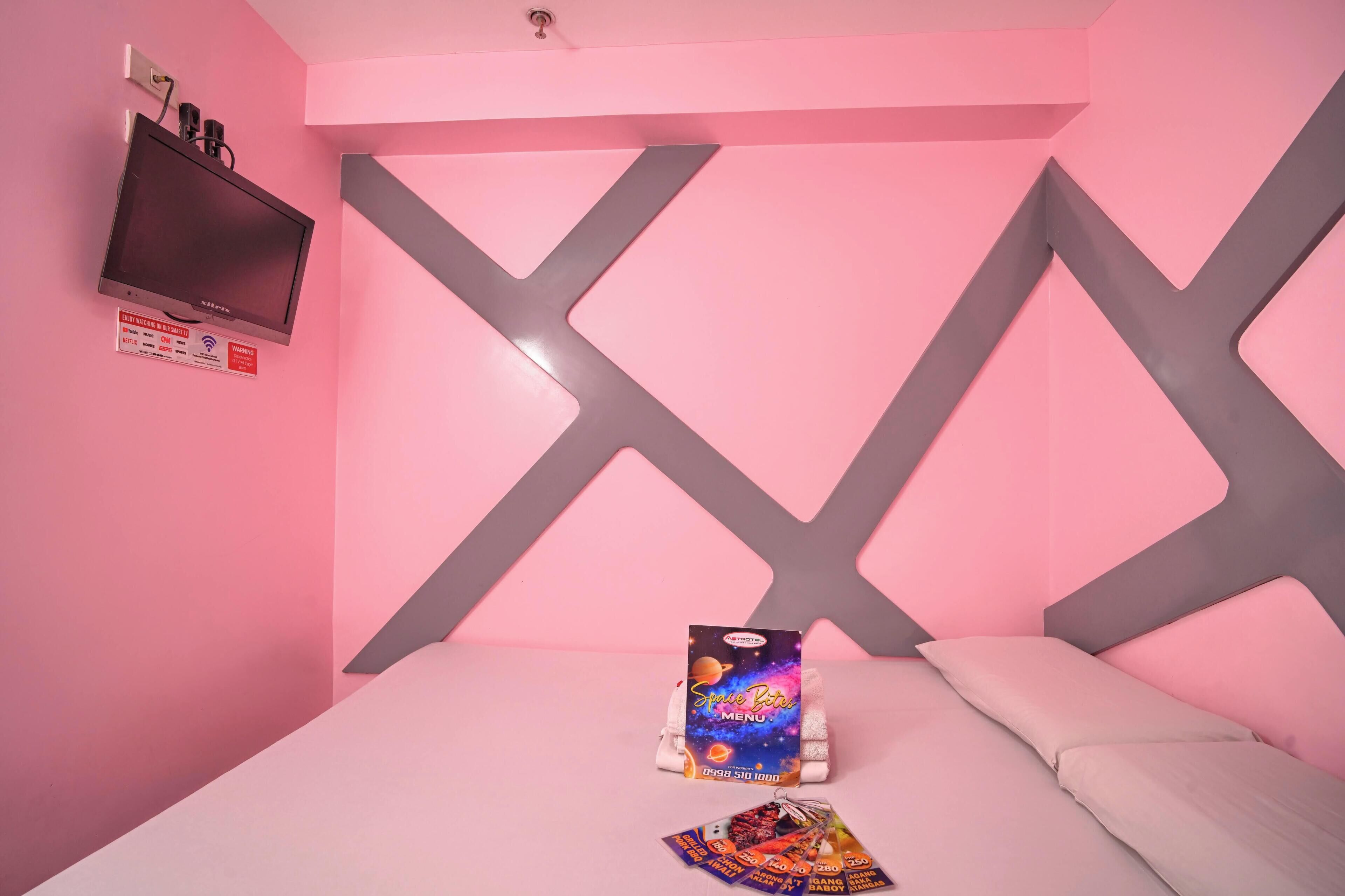A pink-themed room with a bed, a wall-mounted TV, and a menu board.