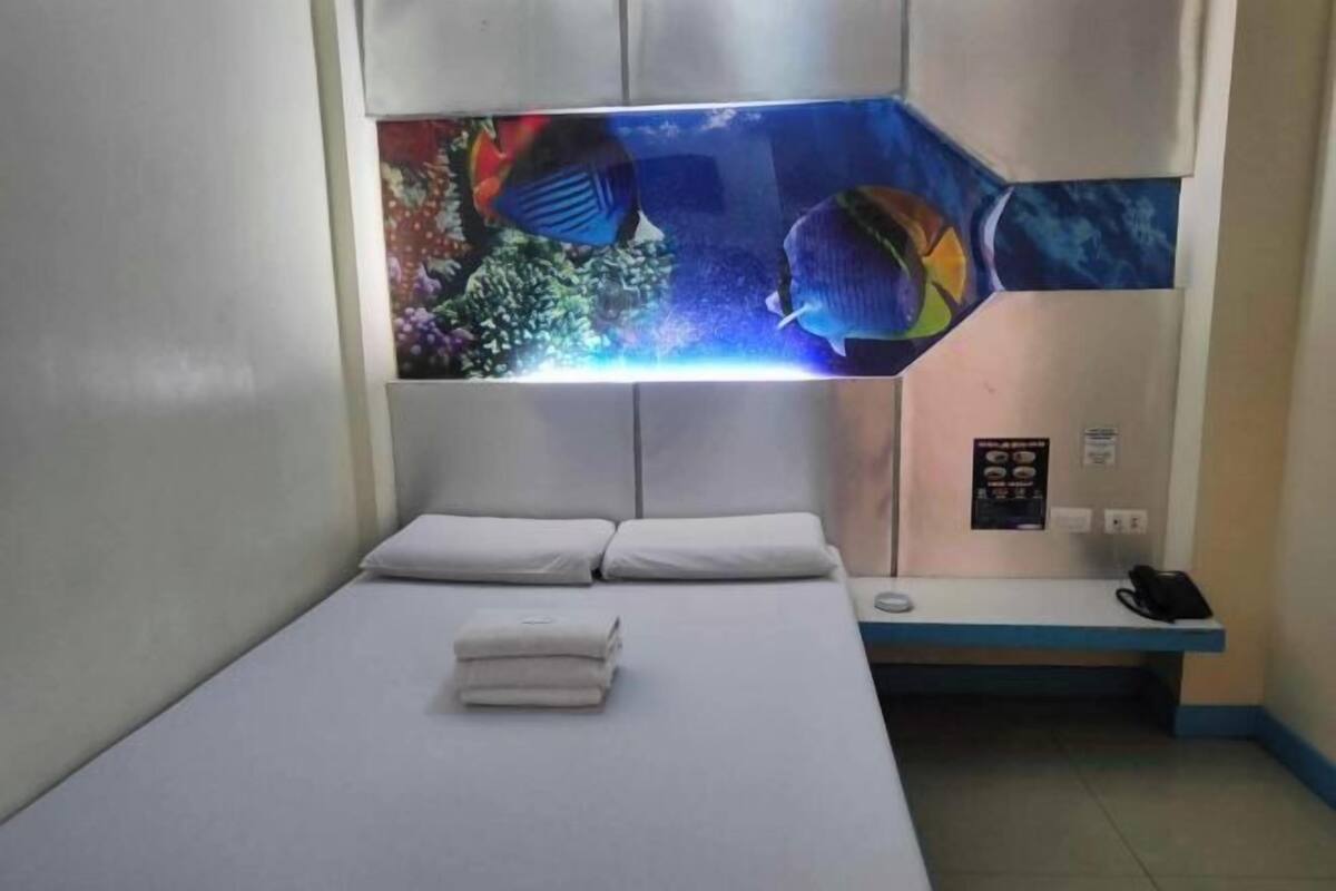 A hotel room with a bed, a headboard with a large aquarium, and a small desk with a phone.