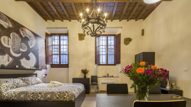 A bedroom with a bed, a desk, a chair, a dining table, and a chandelier.