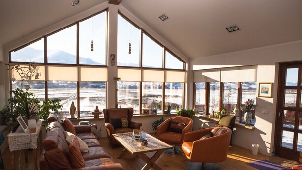 Amplia sala de estar con ventanas grandes, piso de madera y vista a un paisaje nevado.
