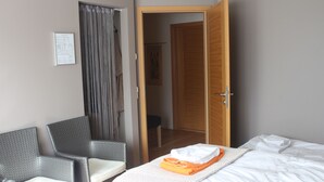 Una habitación de hotel con una cama, una silla, una puerta de madera y una cortina.