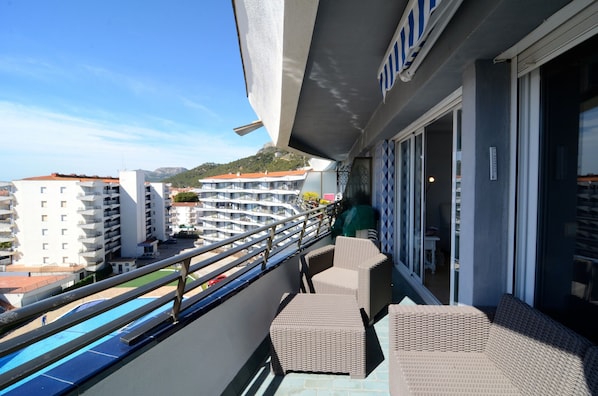 A balcony with wicker furniture, a pool, and buildings in the background.