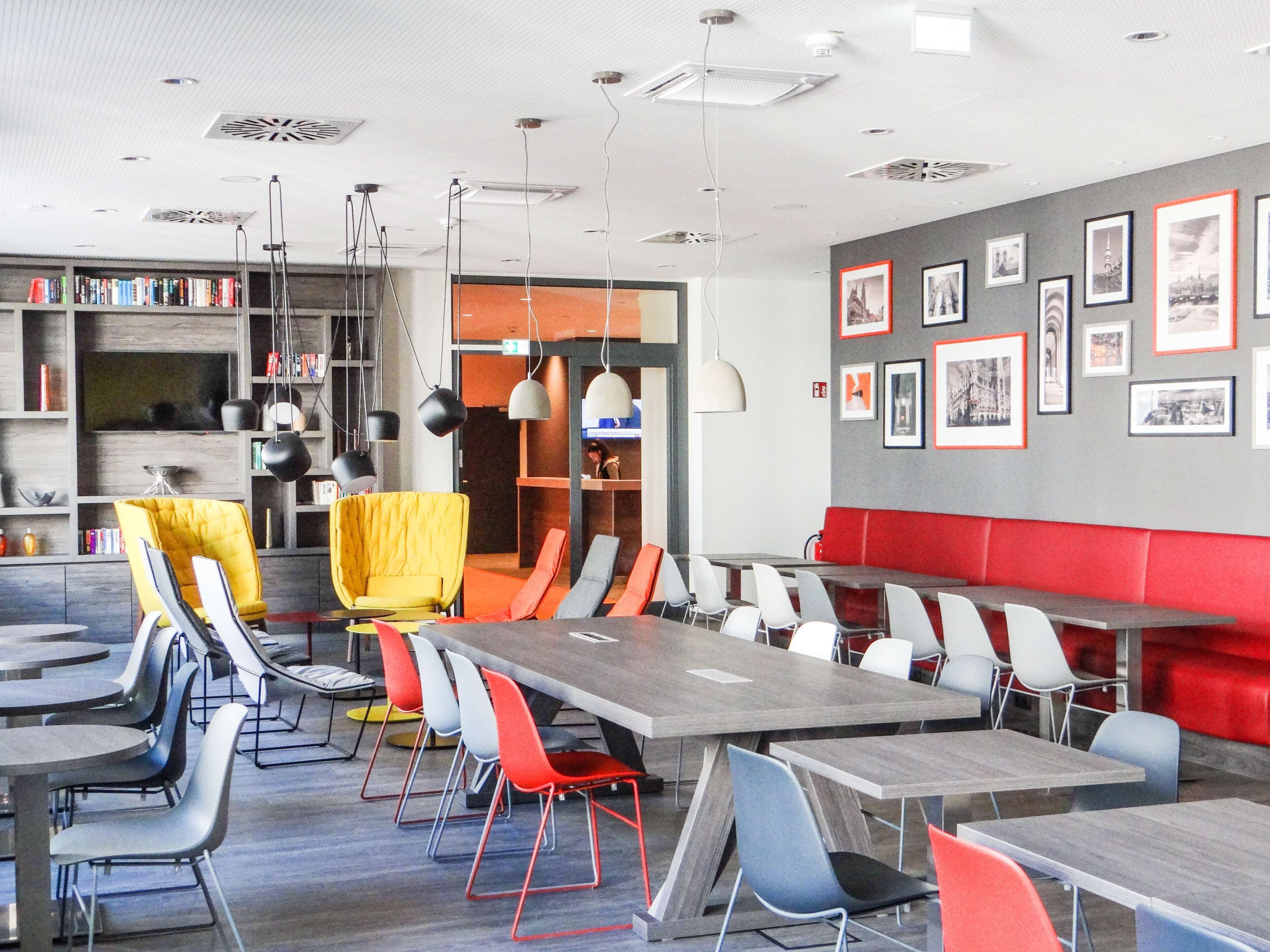 A modern dining area with multiple tables and chairs, a bookshelf, and a wall with framed pictures.