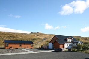 A two-story building with a sloped roof, a small attached garage, and a car parked in front. - Huts in Víðidalur (Hvammstangi)