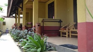 A covered outdoor area with a row of plants, a bench, and a trash bin.