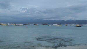 A coastal scene with boats on calm waters and mountains in the background.