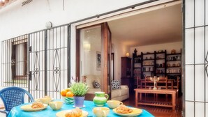 A dining area with a table set for breakfast, including croissants, fruits, and a potted plant.