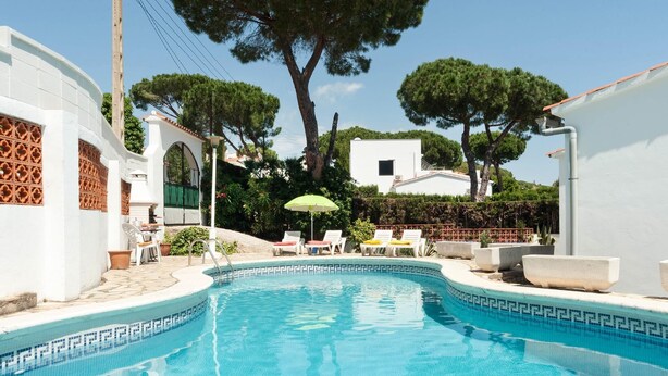 A swimming pool with a tiled edge, surrounded by lounge chairs and a small table.