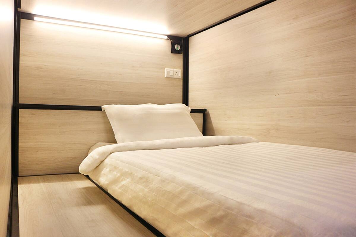 Una cama individual con colchón y almohada blancos, enmarcada en metal negro, en una habitación con paredes de madera y un diseño sencillo y limpio.
