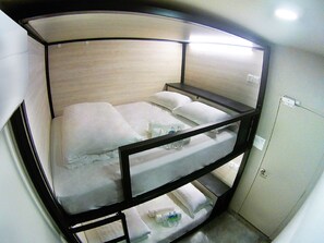A bunk bed with white bedding and a wooden frame. There is a small table with a bottle and a cup on the lower bunk. A white cabinet is visible to the right. - 1992 Capsule Hotel - Hostel (Malacca City)