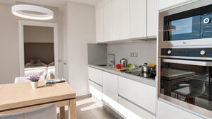 Une cuisine moderne avec des meubles blancs, un four encastré et un coin repas comprenant une table et des chaises en bois.