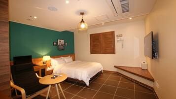 Habitación de hotel con cama, una silla, una mesita, lámpara, televisor y aire acondicionado instalado en la pared.