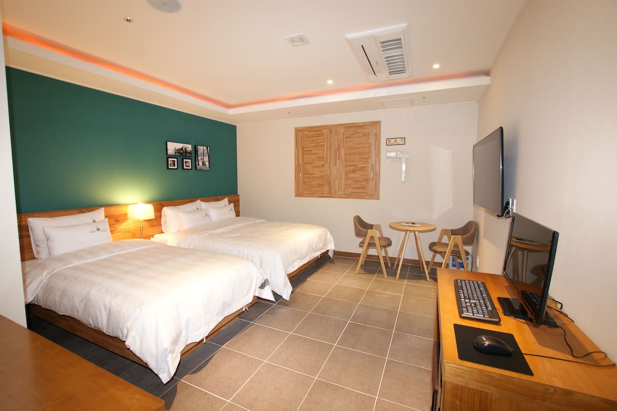 A hotel room with two beds, a desk with a computer, a TV, and a small table with chairs.