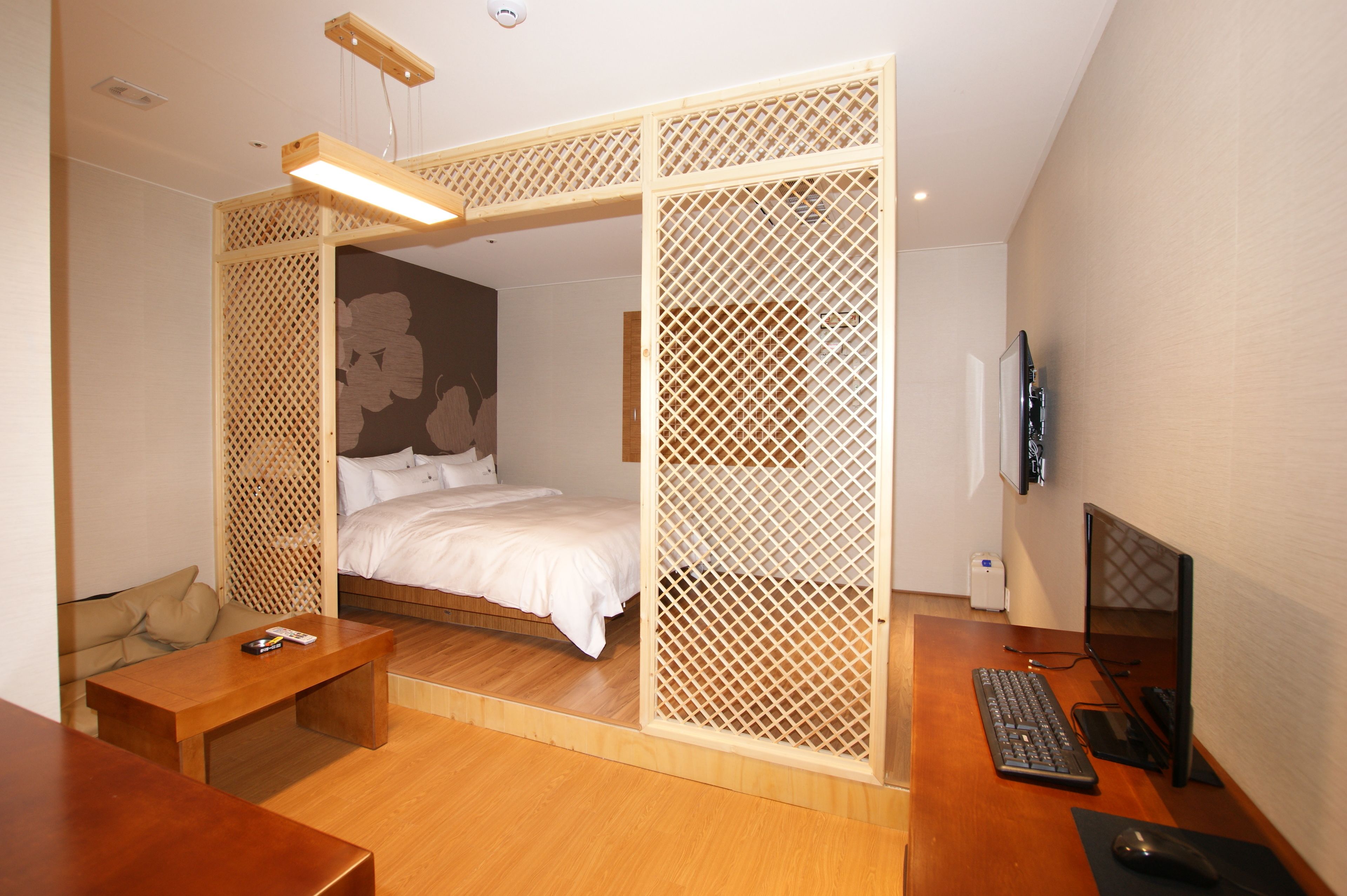A bedroom with a bed, wooden desk, computer, and a TV.