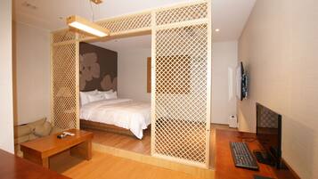 A bedroom with a bed, wooden desk, computer, and a TV.