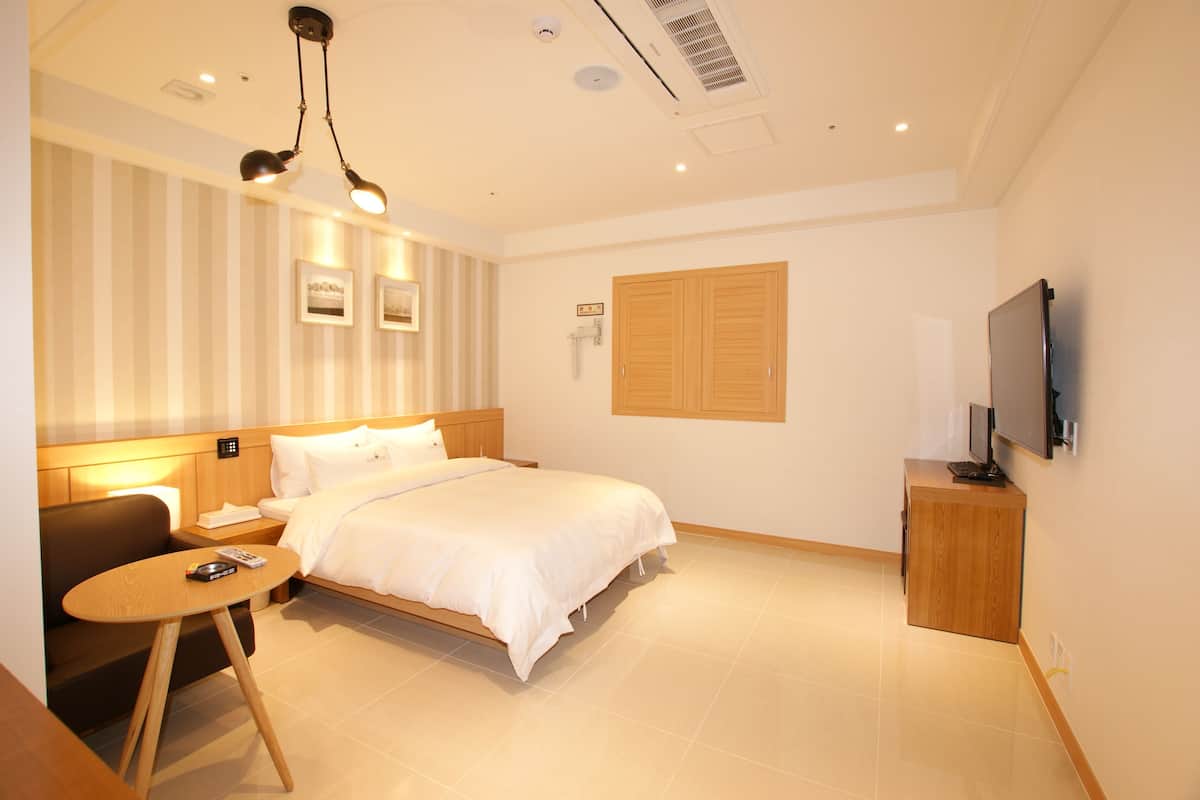A hotel room with a bed, bedside table, TV, and a wooden cabinet.