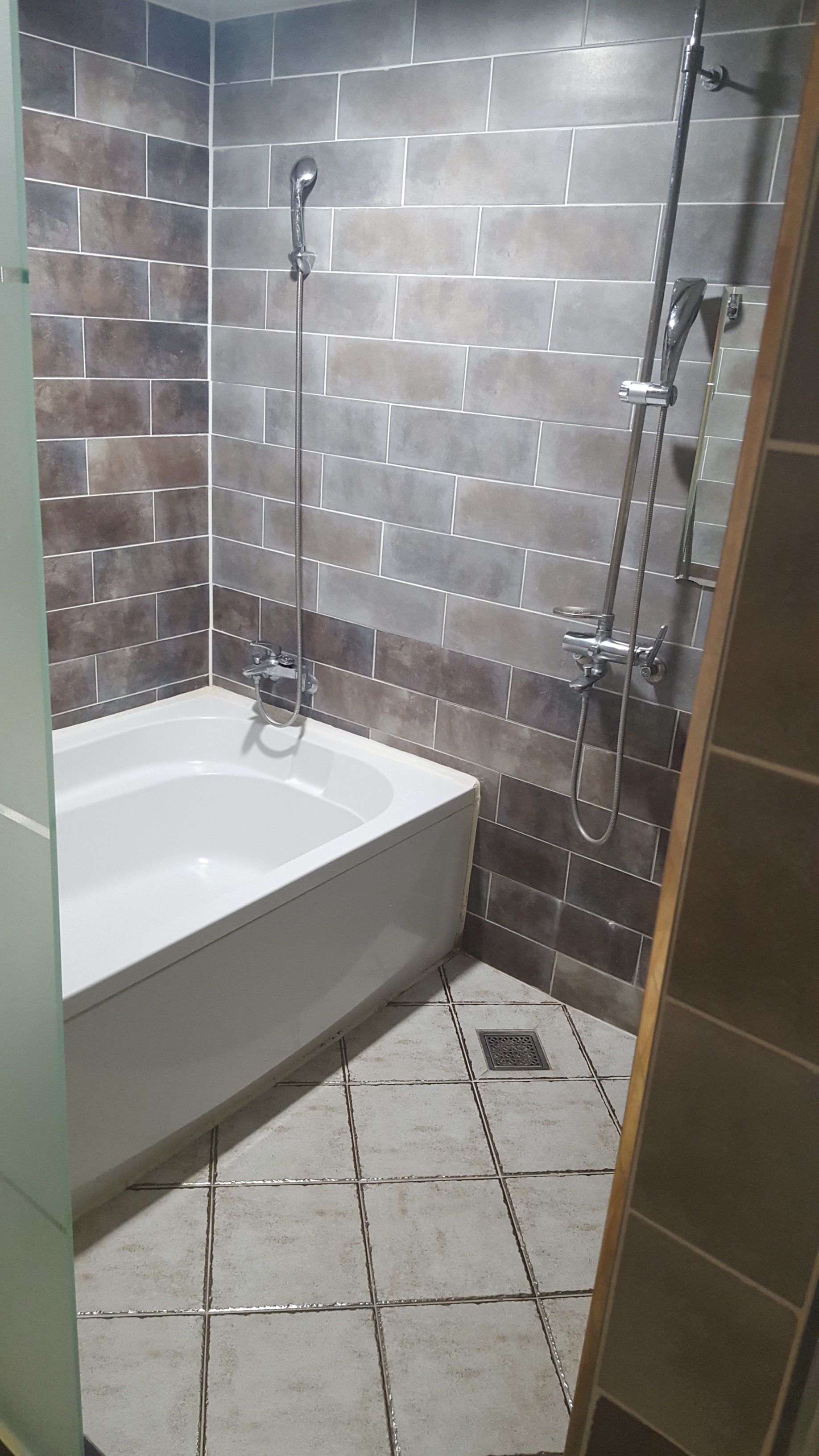 Een badkamer met een bad, douche en betegelde wanden.