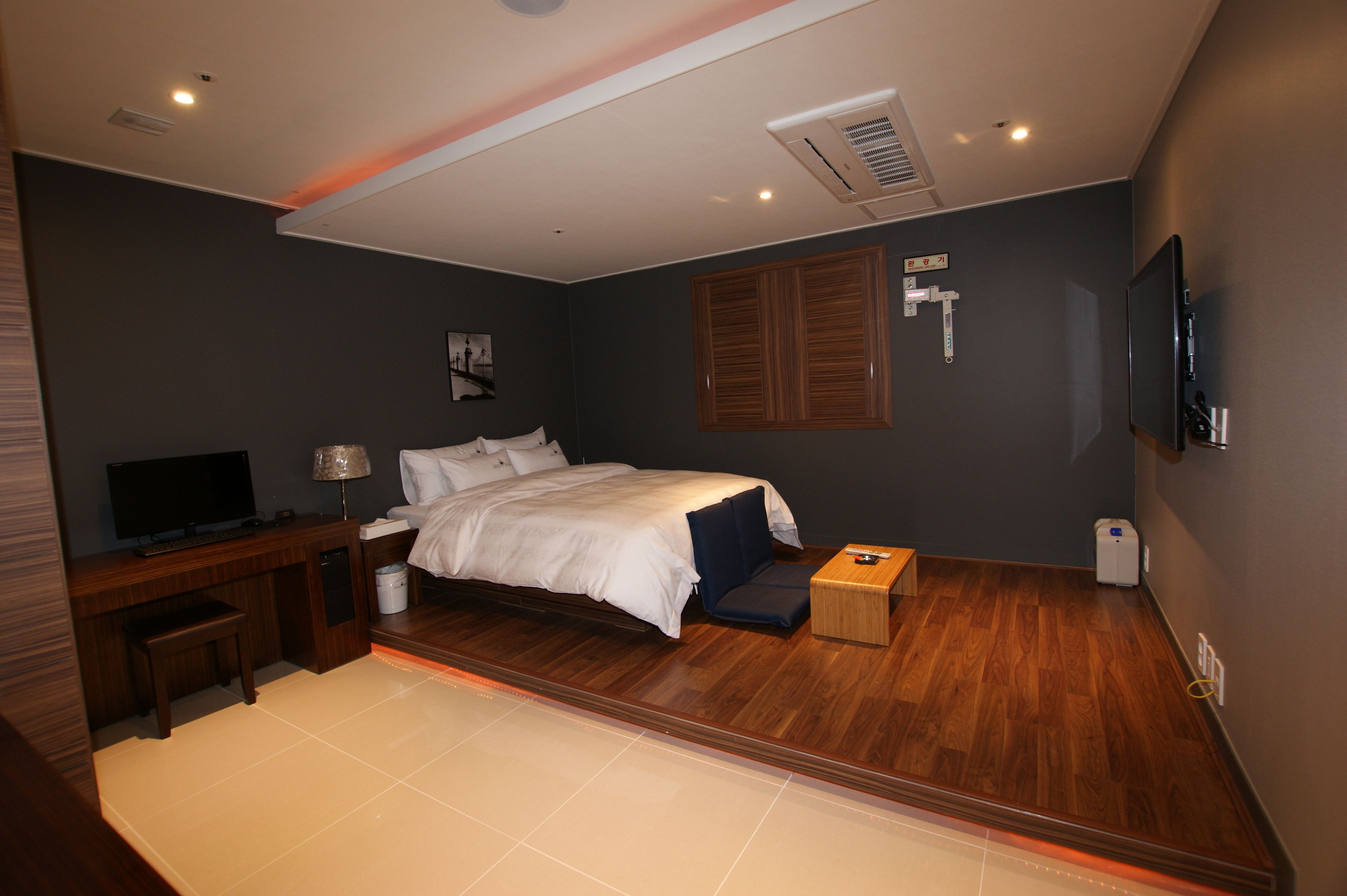 Ein modernes Hotelzimmer mit Bett, Schreibtisch mit Fernseher, einem kleinen Tisch und einem an der Wand befestigten Fernseher.